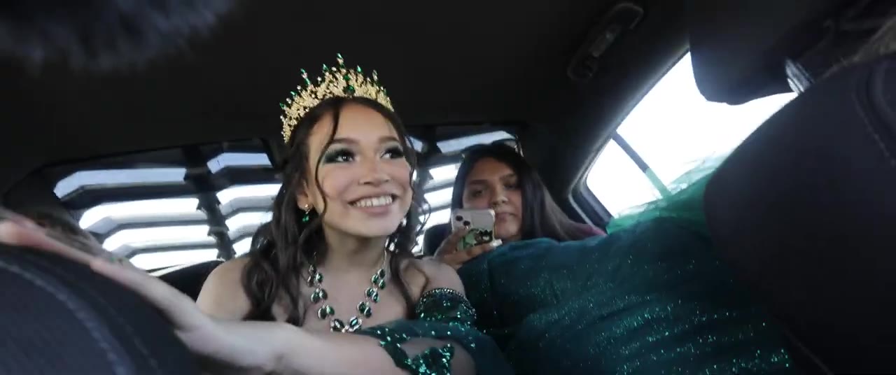 A quincea&ntilde;era in her crown, smiling in the back of a car